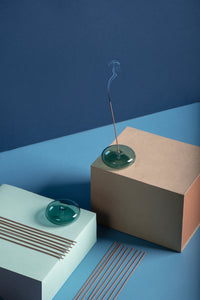 Lit DEEPS Incense Stick sits on blown-glass holder on boxes